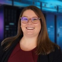 A woman with brown hair and glasses smiles at the camera in front of a blurred background of server racks.