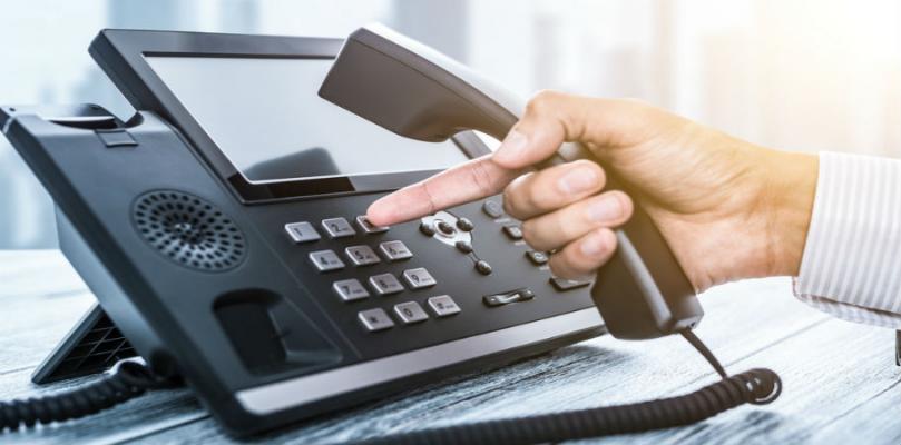 A person's hand is dialing a number on a modern office phone.