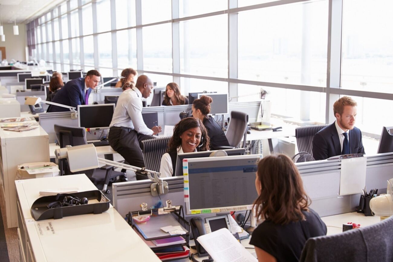 A diverse group of professionals work in a modern, open-plan office with large windows.