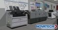 A modern office space features multiple large printing and copying machines, along with a logo for
